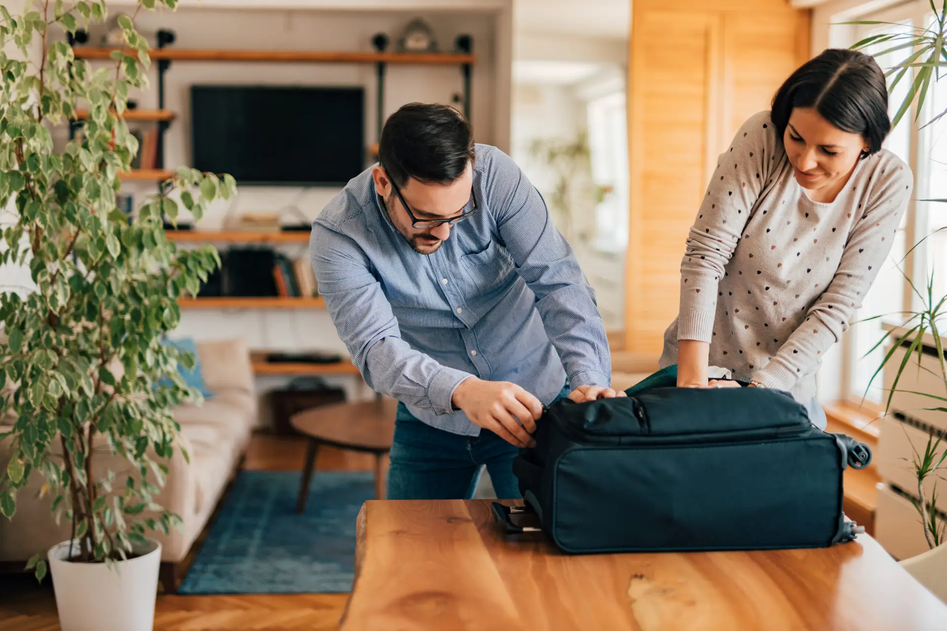 Couple trying to close suitcase, preparing for vacation.