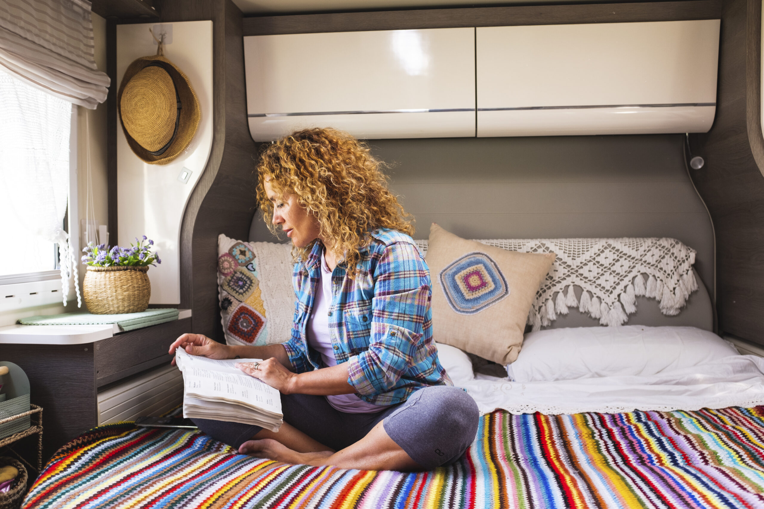 One woman reading a book comfortably sitting on bed inside a camper van modern motorhome alternative tiny cozy house. Relaxation and indoor leisure activity people lifestyle. Travel and vanlife lady